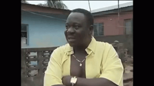 A Man Wearing A Yellow Shirt And A Watch Is Standing In Front Of A Building . GIF