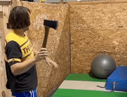A Man Wearing A Yellow Shirt That Says This Is Holding An Axe In Front Of A Wooden Wall . GIF