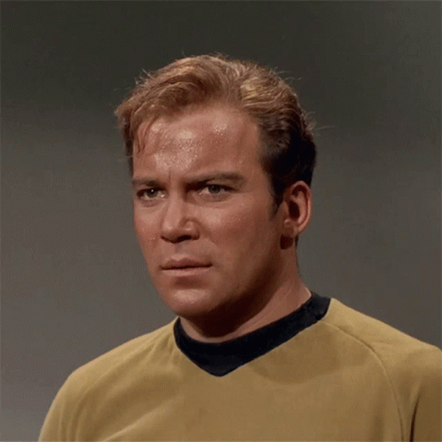 A Man Wearing A Yellow Shirt With A Black Collar Looks At The Camera GIF