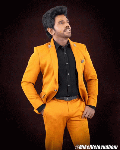 A Man Wearing A Yellow Suit And A Black Shirt Is Standing With His Hands In His Pockets And The Hashtag Mikelvelayudham GIF