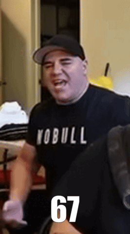 A Man Wearing A Yobull Shirt And A Hat Is Standing In A Room GIF