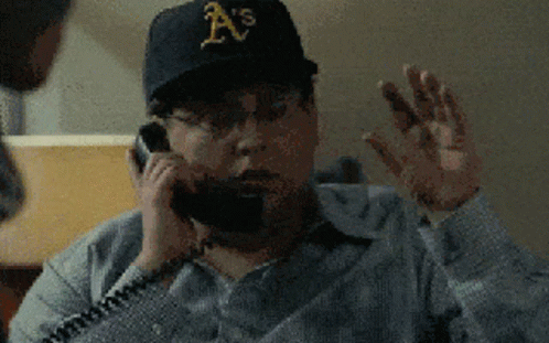 A Man Wearing An A 'S Hat Is Talking On A Telephone GIF