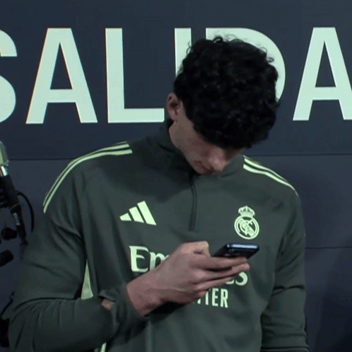 a man wearing an adidas shirt looks at his cell phone