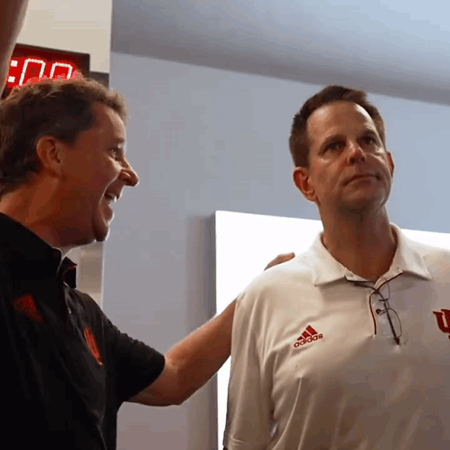 A Man Wearing An Adidas Shirt Stands Next To A Man Wearing A Black Shirt GIF