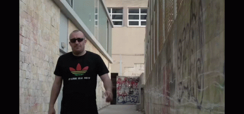a man wearing an adidas t-shirt walks down a street