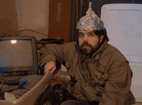 A Man Wearing An Aluminum Foil Hat Sits In A Bin GIF
