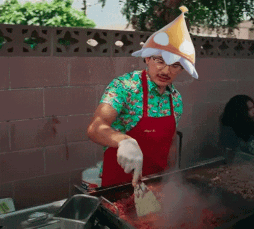 A Man Wearing An Apron And A Party Hat Is Cooking GIF