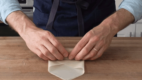 A Man Wearing An Apron Is Folding A Piece Of Paper GIF