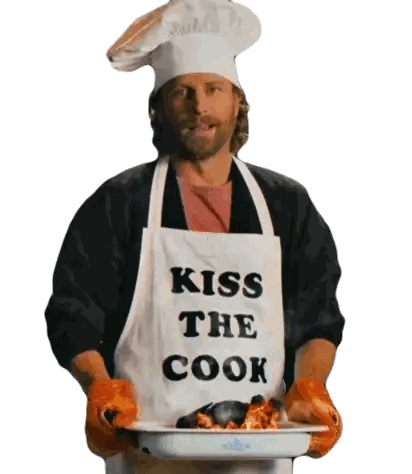 a man wearing an apron that says kiss the cook is holding a pan of food