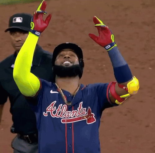 A Man Wearing An Atlanta Baseball Jersey Holds His Arms Up In The Air GIF