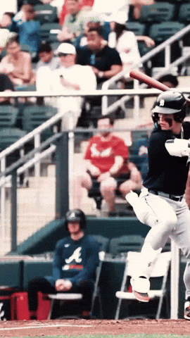 A Man Wearing An Atlanta Shirt Sits In The Dugout Watching A Baseball Player Swing His Bat GIF