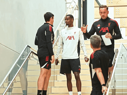 a man wearing an aya shirt talks to another man on the stairs