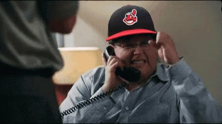 A Man Wearing An Indians Hat Is Talking On A Telephone GIF