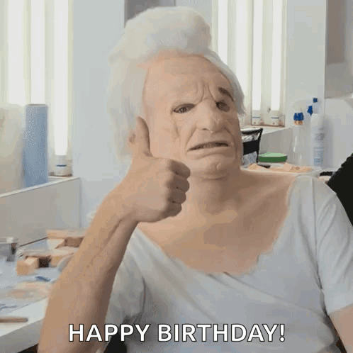 A Man Wearing An Old Woman 'S Mask Giving A Thumbs Up With The Words Happy Birthday Behind Him GIF