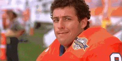 A Man Wearing An Orange Football Jersey With The Number 8 On It Is Looking At The Camera . GIF