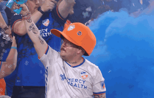 A Man Wearing An Orange Hat And A Mercy Health Shirt GIF