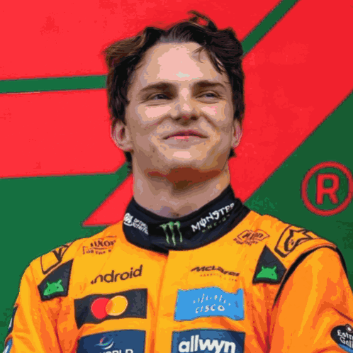 A Man Wearing An Orange Racing Suit With Monster Energy And Allwyn Logos GIF