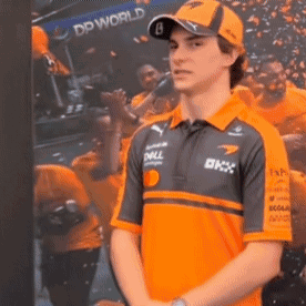 A Man Wearing An Orange Shirt And A Hat Is Standing In Front Of A Picture Of A Crowd . GIF