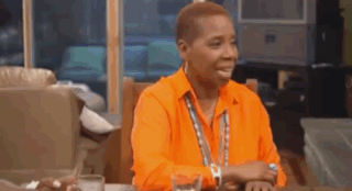 A Man Wearing An Orange Shirt Is Sitting At A Table With A Glass Of Water . GIF