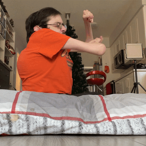 A Man Wearing An Orange Shirt That Says ' Ucsd ' On It Sits On A Bed GIF