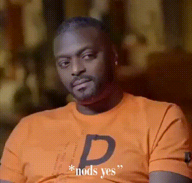 A Man Wearing An Orange Shirt With The Letter D On It Is Sitting Down . GIF