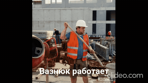 A Man Wearing An Orange Vest And A White Hard Hat Is Standing In Front Of A Concrete Mixer On A Construction Site GIF