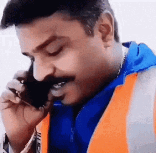 A Man Wearing An Orange Vest Is Talking On A Cell Phone . GIF