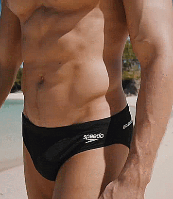 A Man Wearing Black Speedo Swim Briefs Is Standing On A Beach GIF