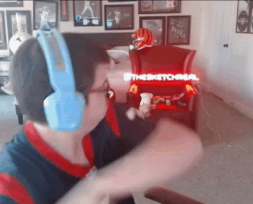 A Man Wearing Blue Headphones Is Sitting In Front Of A Chair That Says " Thesketchman " GIF