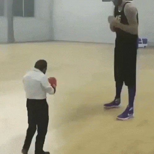 A Man Wearing Boxing Gloves Is Standing Next To A Man Wearing Basketball Shorts On A Basketball Court . GIF