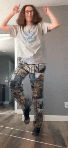 A Man Wearing Camo Pants Is Jumping In The Air With His Hands In The Air GIF