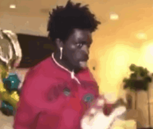 A Man Wearing Ear Buds And A Red Shirt Is Standing In A Room . GIF