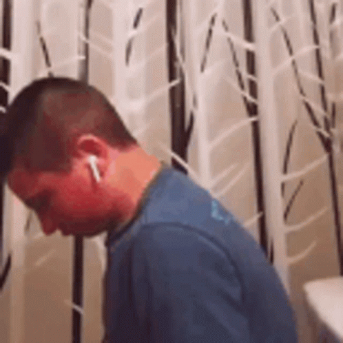 A Man Wearing Ear Buds Is Standing In Front Of A Wall With Trees Painted On It . GIF