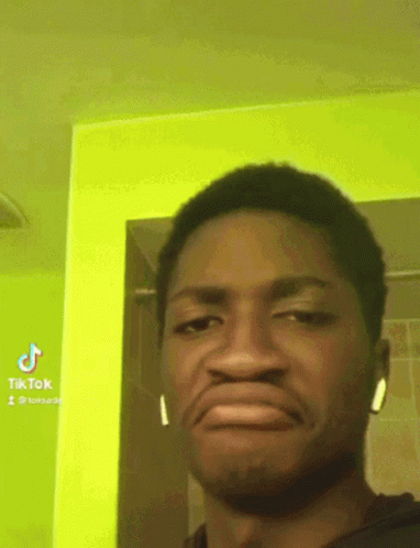 A Man Wearing Ear Buds Making A Funny Face In Front Of A Green Wall GIF