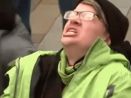 A Man Wearing Glasses , A Green Jacket And A Black Hat Is Making A Funny Face . GIF
