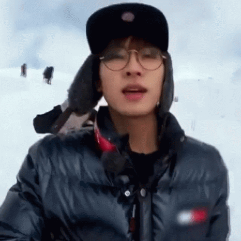A Man Wearing Glasses , A Hat And A Jacket Is Standing In The Snow . GIF