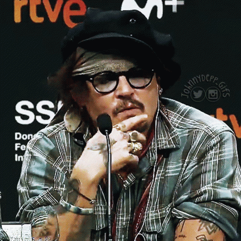 A Man Wearing Glasses And A Bandana Talks Into A Microphone In Front Of A Sign That Says Rtve Ss GIF