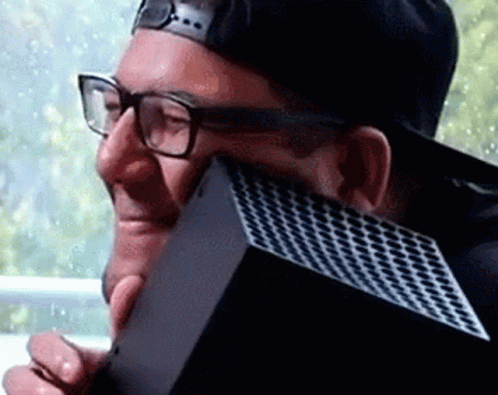 A Man Wearing Glasses And A Baseball Cap Is Holding A Xbox Box . GIF