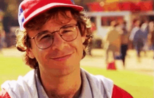 A Man Wearing Glasses And A Baseball Cap Is Smiling At The Camera . GIF