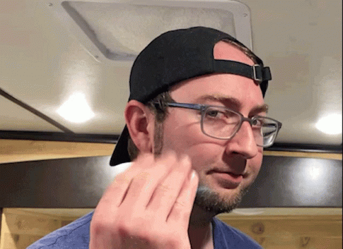 A Man Wearing Glasses And A Baseball Cap Wipes His Face GIF