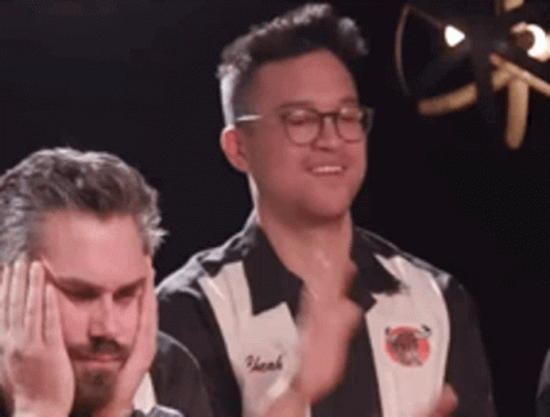 A Man Wearing Glasses And A Black And White Shirt Is Clapping His Hands . GIF