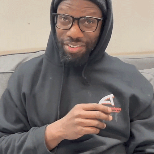 A Man Wearing Glasses And A Black Hoodie Holds A Small Object GIF