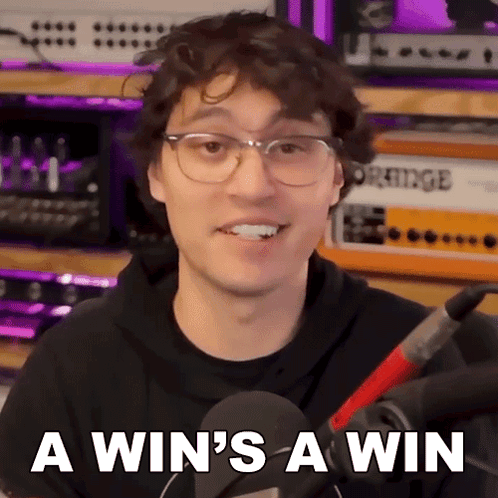 A Man Wearing Glasses And A Black Hoodie Says " A Win 'S A Win " In Front Of A Microphone GIF