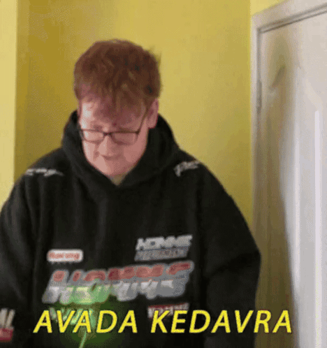 A Man Wearing Glasses And A Black Hoodie That Says Avada Kedavra GIF