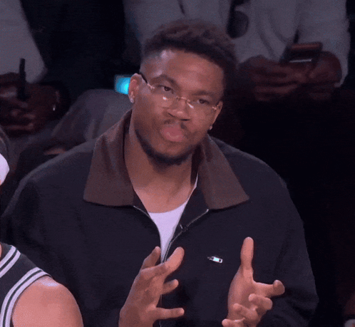 A Man Wearing Glasses And A Black Jacket Has His Hands Up GIF
