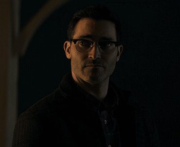 A Man Wearing Glasses And A Black Jacket Stands In The Dark GIF