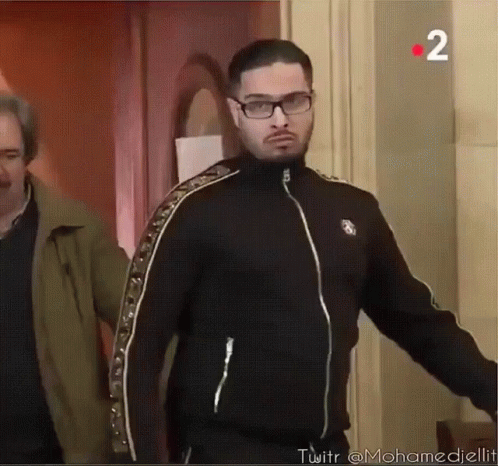 A Man Wearing Glasses And A Black Jacket With The Number 2 In The Corner GIF