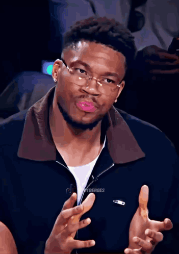 A Man Wearing Glasses And A Black Jacket With The Word Lacoste On It GIF