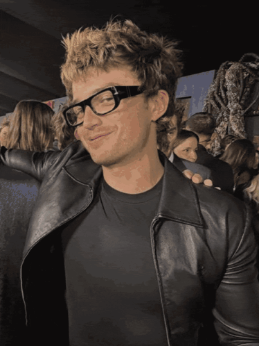 A Man Wearing Glasses And A Black Leather Jacket Smiles GIF