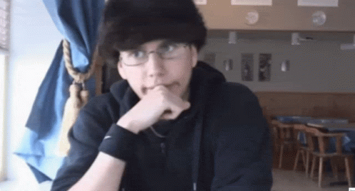 A Man Wearing Glasses And A Black Nike Wristband Is Sitting At A Table GIF